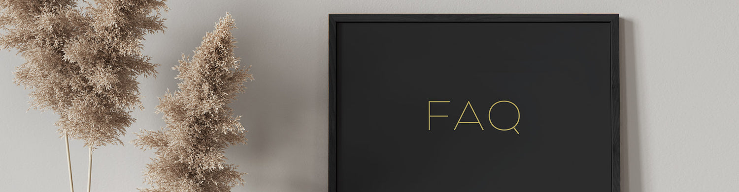 A framed 'FAQ' sign in gold lettering on a black background, hung on a wall beside pampas grass.